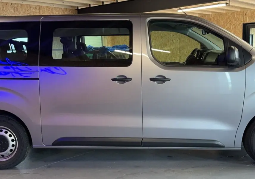 Profil côté gauche d'un Opel Vivaro Combi gris 2022 avec vitres teintées et jantes acier en intérieur d'atelier.