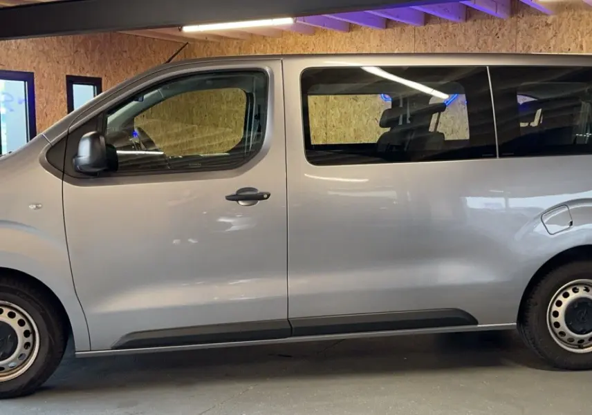 Profil côté gauche d'un Opel Vivaro Combi gris 2022 avec jantes acier et grandes fenêtres teintées.