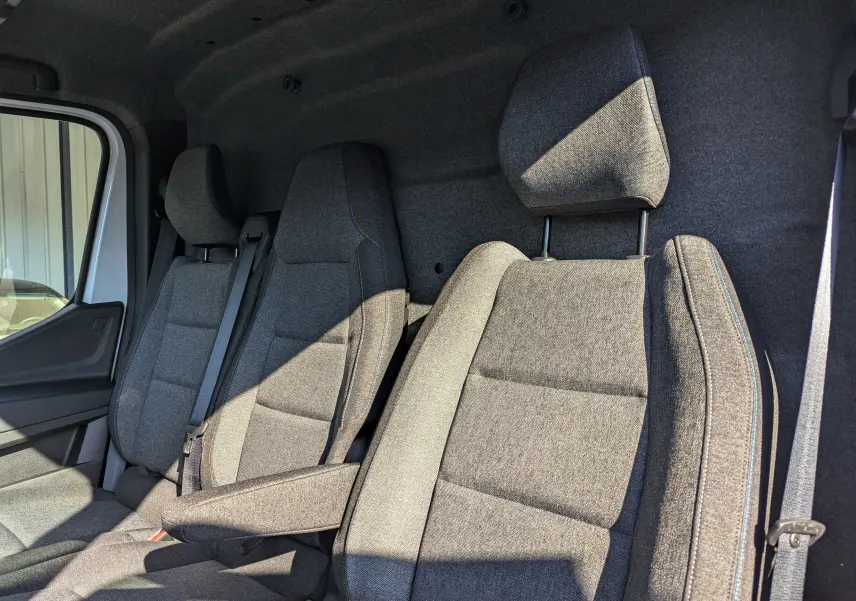 Intérieur du Renault Master 2025 montrant les sièges en tissu gris côté conducteur et passager, avec accoudoir côté droit.