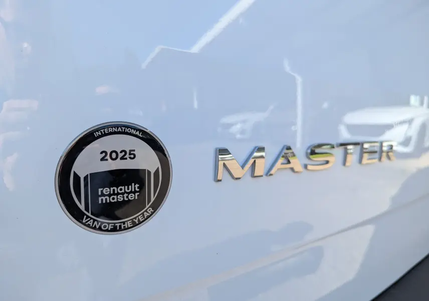 Gros plan sur l'écusson "Van of the Year 2025" et le logo chromé MASTER sur la carrosserie blanche du Renault Master.