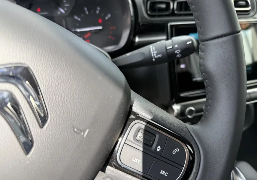 Gros plan sur le volant cuir noir d'une Citroën C3 gris platinium 2024 avec commandes audio intégrées.