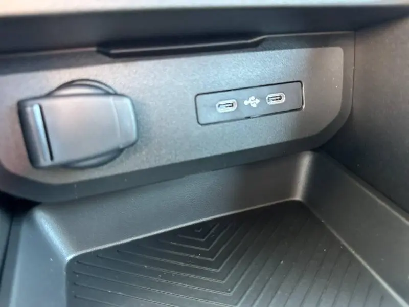 Prise USB double et prise 12V noires intégrées dans la console centrale du Dacia Duster blanc 2025.