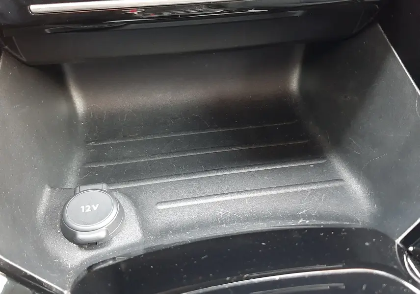 Gros plan sur la prise 12V et le rangement central noir brillant de la Peugeot 2008 Hybrid 145 Allure 2025.