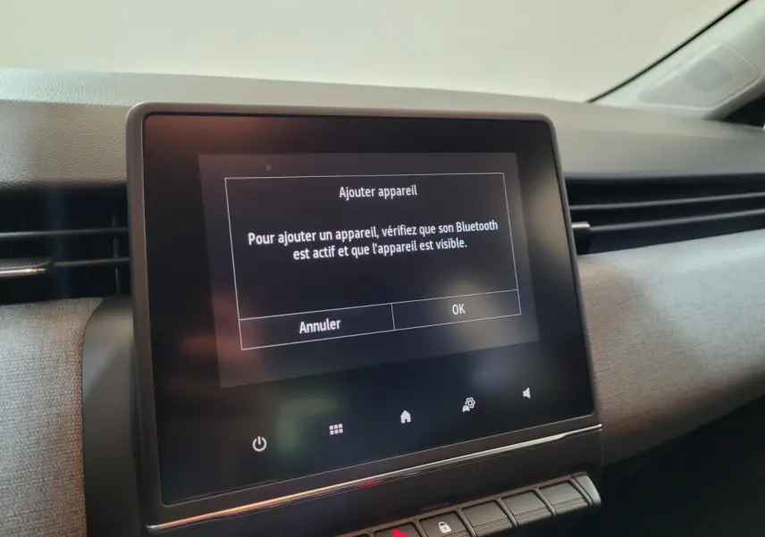 Écran tactile central affichant un message Bluetooth dans l’habitacle clair d’une Renault Clio gris foncé.