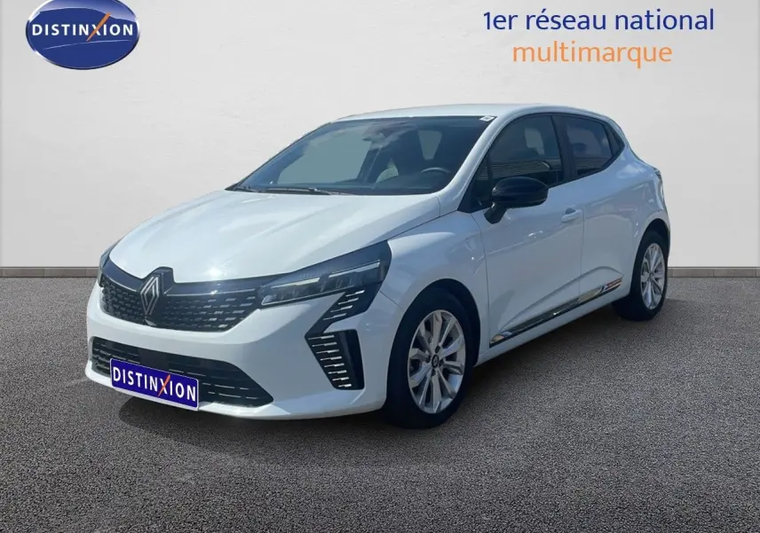 Renault Clio blanche vue 3/4 avant droit, avec calandre noire et feux LED distinctifs, stationnée devant un mur clair.