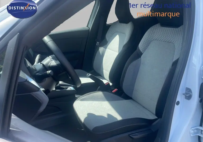 Vue intérieure côté conducteur de la Renault Clio blanche 2025, mettant en valeur les sièges tissu gris et noir et le volant multifonction.