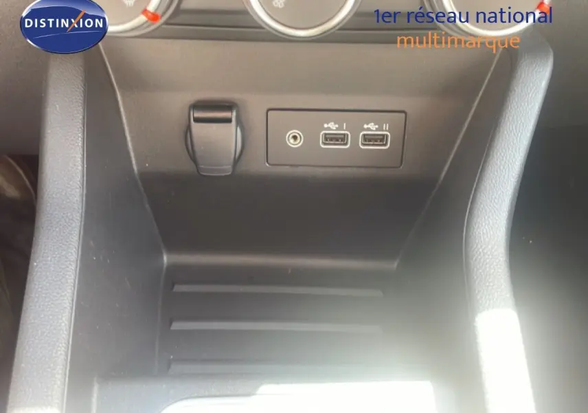 Vue rapprochée de la console centrale noire de la Renault Clio blanche, montrant les ports USB et prise auxiliaire.