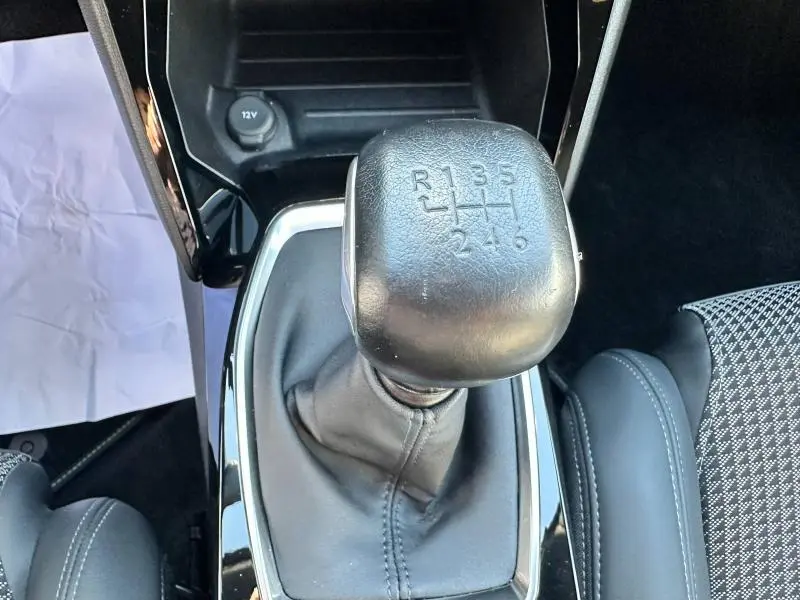 Gros plan sur le levier de vitesses manuel noir du Peugeot 2008 gris Artense, entouré de sellerie tissu et cuir.