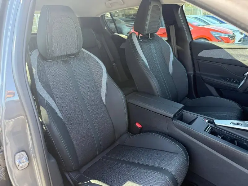 Vue intérieure côté avant gauche du Peugeot 308 gris 2025, sièges tissu et cuir avec surpiqûres contrastées.