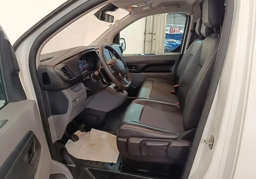 Vue intérieure côté conducteur du Citroën Jumpy blanc, montrant les sièges noirs et le tableau de bord moderne.