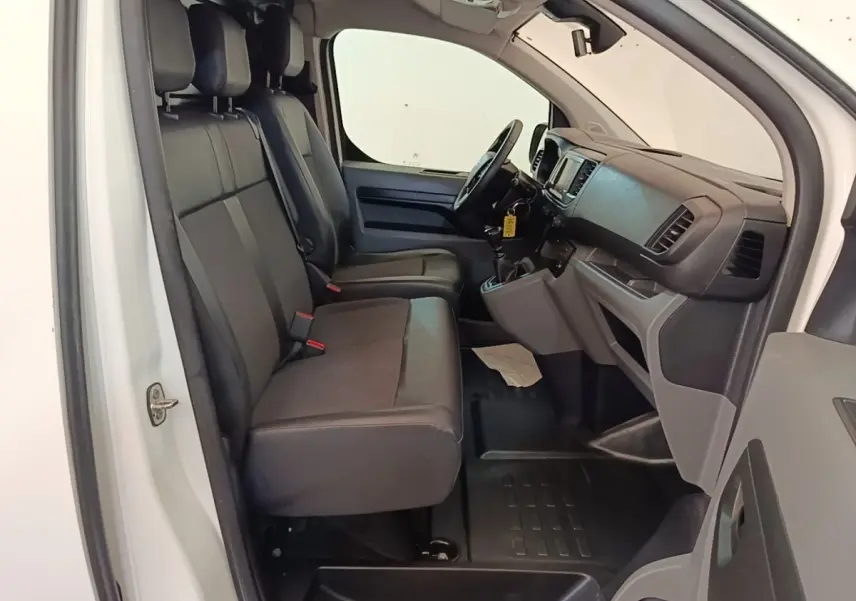 Vue intérieure côté conducteur du Citroën Jumpy blanc, montrant les sièges avant et le tableau de bord noir.