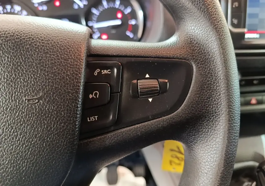 Gros plan sur le volant noir du Citroën Jumpy blanc, avec commandes audio et tableau de bord flou en arrière-plan.