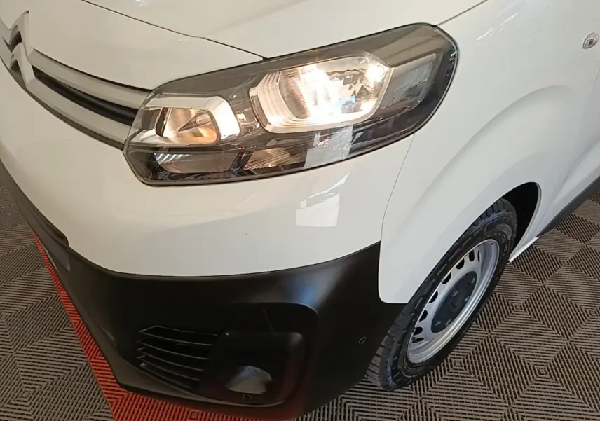 Vue rapprochée 3/4 avant droit du Citroën Jumpy blanc avec phares allumés et pare-chocs noir mat.