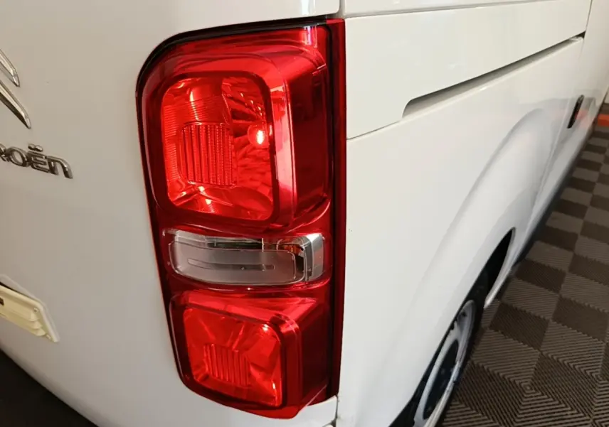 Gros plan sur le feu arrière gauche rouge d’un Citroën Jumpy blanc, avec partie latérale et roue visible.