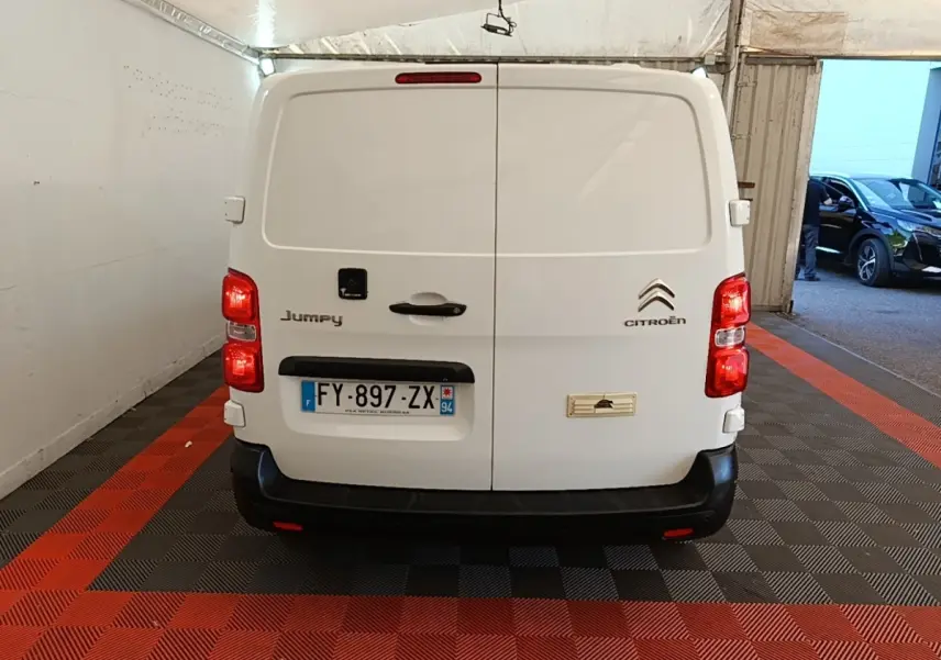 Vue arrière d’un utilitaire Citroën Jumpy blanc, portes battantes fermées avec plaques et feux rouges visibles.
