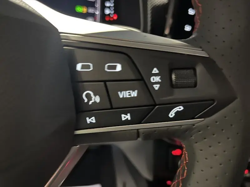 Gros plan sur les commandes multifonctions du volant perforé avec surpiqûres rouges d'une SEAT Ibiza blanche 2024.