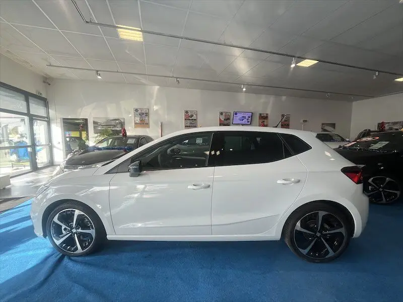 Profil droit d'une SEAT IBIZA 2024 blanc Nevada Metal avec jantes noires bicolores en showroom.