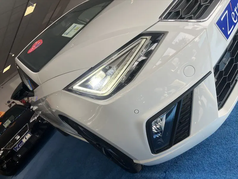 Vue 3/4 avant droit d'une SEAT Ibiza 2024 blanche Nevada Metal avec phares LED allumés et calandre hexagonale.