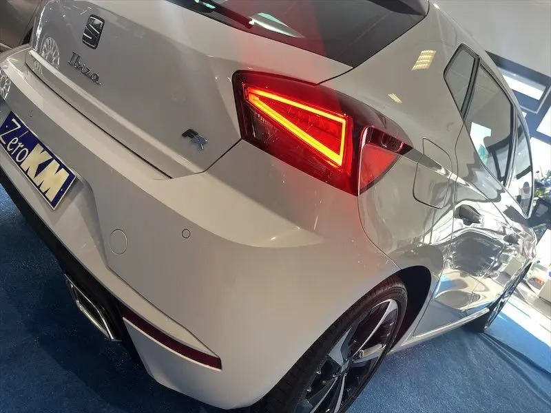 Vue 3/4 arrière droite d'une SEAT Ibiza FR Sport blanche Nevada Metal avec feux LED allumés et jantes noires biton.