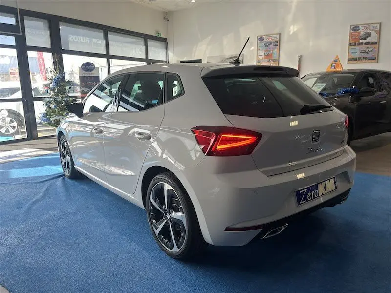 SEAT Ibiza blanc Nevada métal vue 3/4 arrière droit en showroom avec jantes noires et rouges allumées.