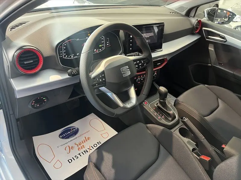 Intérieur avant droit de la SEAT IBIZA 1.5 TSI 150CH DSG FR SPORT 2024 avec volant multifonction et garnitures rouges.