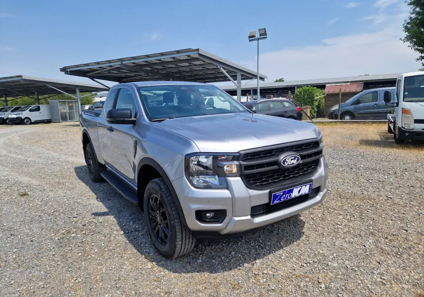 Ford Ranger Super Cabine gris iconic vu en 3/4 avant droit, avec marchepieds et jantes noires sur parking extérieur.