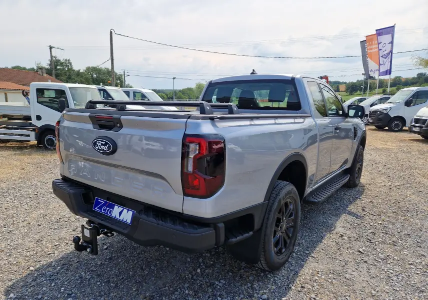 Ford Ranger Super Cabine gris Iconic vu en 3/4 arrière droit, avec marchepied, barres de plateau et attelage visible.