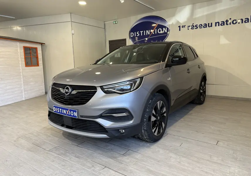 Opel Grandland X gris Himalaya vu en 3/4 avant droit, intérieur showroom avec logo Distinxion en arrière-plan.