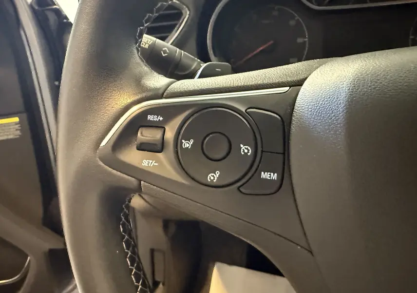 Gros plan sur les commandes de régulateur de vitesse au volant d'un Opel Grandland X hybride gris Himalaya.