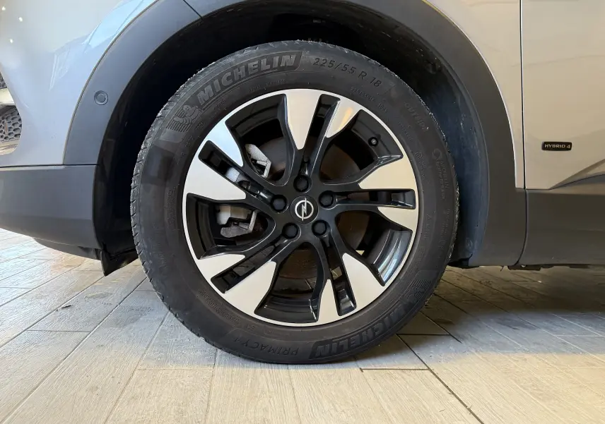Gros plan sur la roue avant gauche d'un Opel Grandland X gris Himalaya avec jante alliage bicolore et badge Hybrid 4.