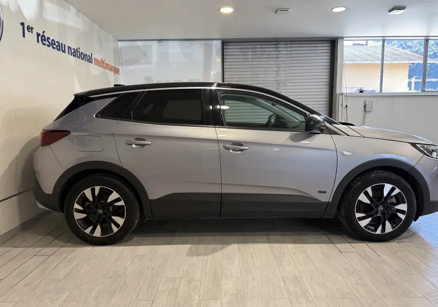 Profil côté gauche d'un Opel Grandland X gris Himalaya avec jantes noires et toit noir en intérieur showroom.