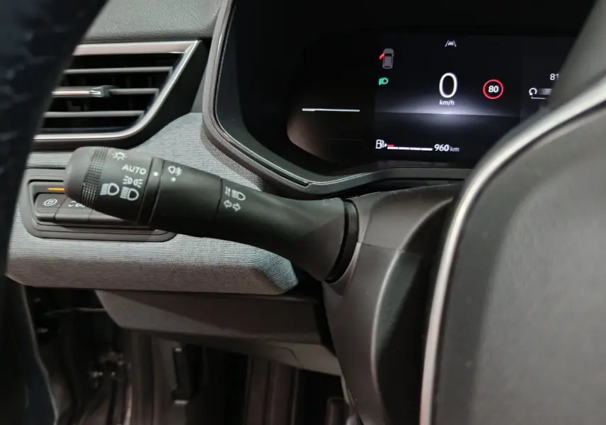 Gros plan sur le combiné d'instruments numérique et la commande des phares à gauche du volant dans une Renault Clio gris clair de 2025.