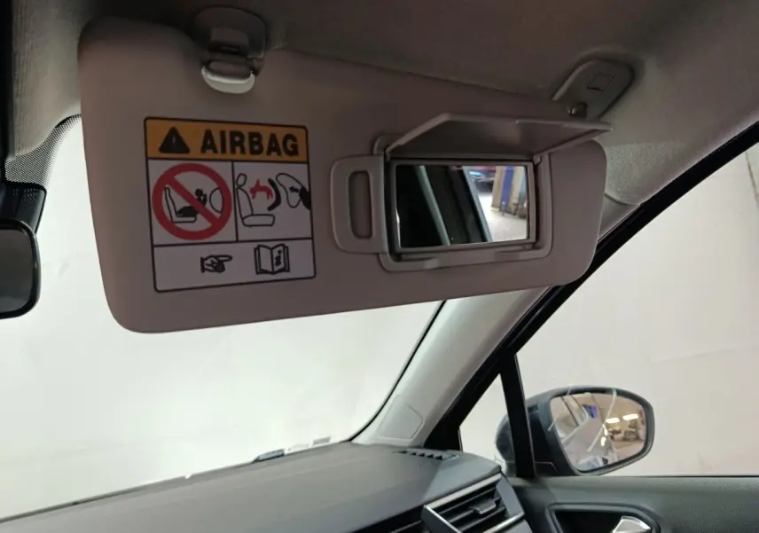 Vue intérieure côté conducteur de la Renault Clio gris clair 2025, pare-soleil avec miroir et avertissement airbag visible.