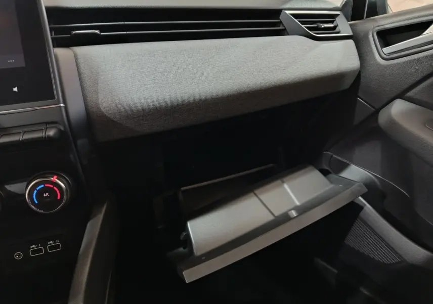 Vue intérieure côté passager de la Renault Clio 2025 gris clair, avec boîte à gants ouverte et tableau de bord textile.