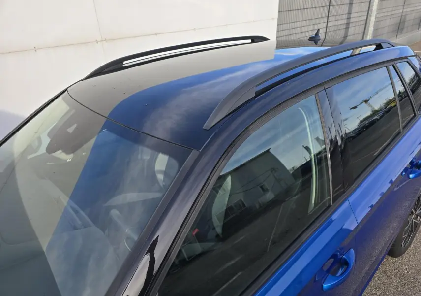 Vue plongeante côté droit du Skoda Kamiq 2025 bleu racing avec toit noir et barres de toit noires.