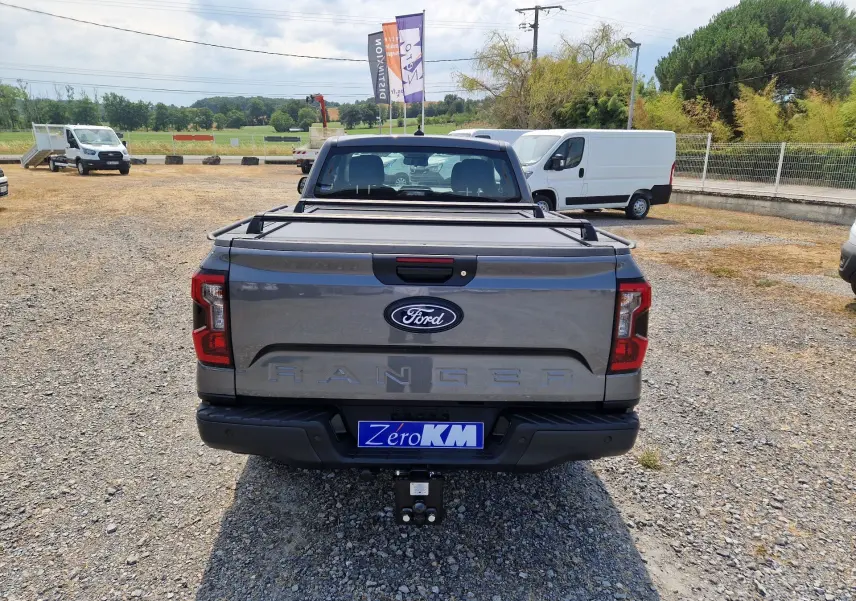 Vue arrière d’un Ford Ranger Super Cabine gris carbone avec rideau de plateau rigide et attelage visible.