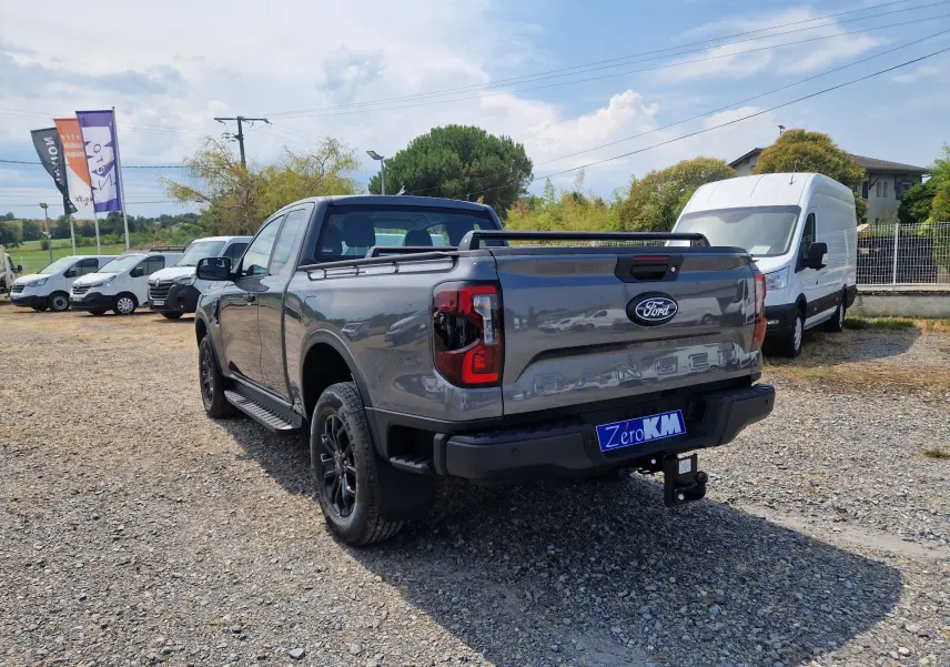 Vue 3/4 arrière droite du Ford Ranger Super Cabine gris carbone avec plateau et barres de toit visibles.