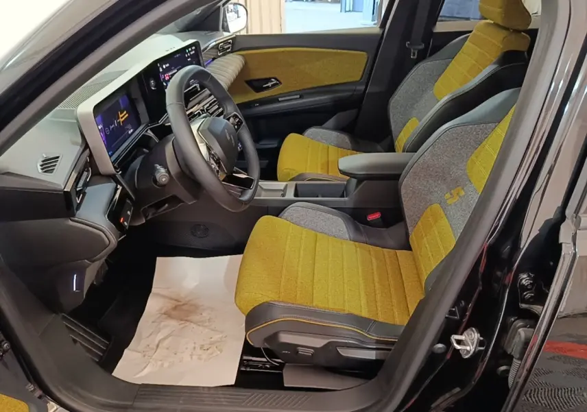 Vue intérieure côté conducteur de la Renault R5 Iconic 2024, sièges tissu jaune et gris avec tableau de bord numérique.