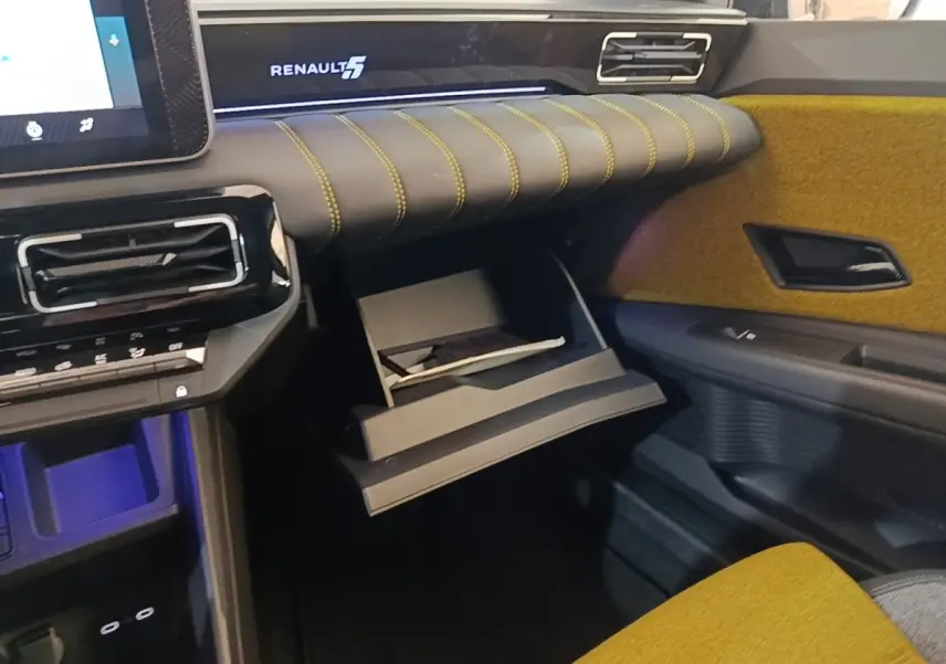 Intérieur Renault 5 Iconic 2024 côté passager, tableau de bord noir avec surpiqûres jaunes et boîte à gants ouverte.