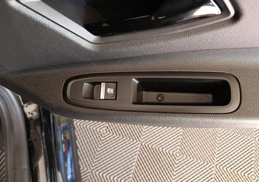 Gros plan sur la commande de lève-vitre côté gauche de la porte intérieure d’une Renault R5 électrique 2024 noire.
