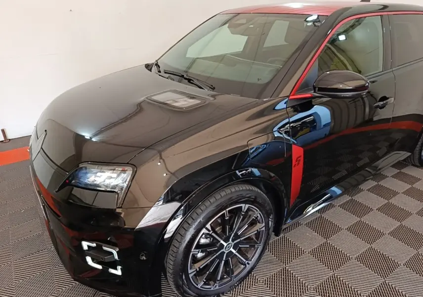 Vue 3/4 avant droite de la Renault R5 Iconic électrique noire avec toit et détails rouges, jantes noires distinctives.
