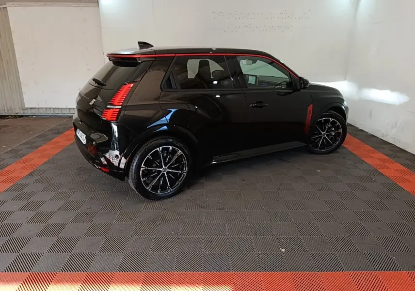 Vue 3/4 arrière droite de la Renault R5 Iconic électrique noire avec détails rouges et jantes noires en intérieur showroom.