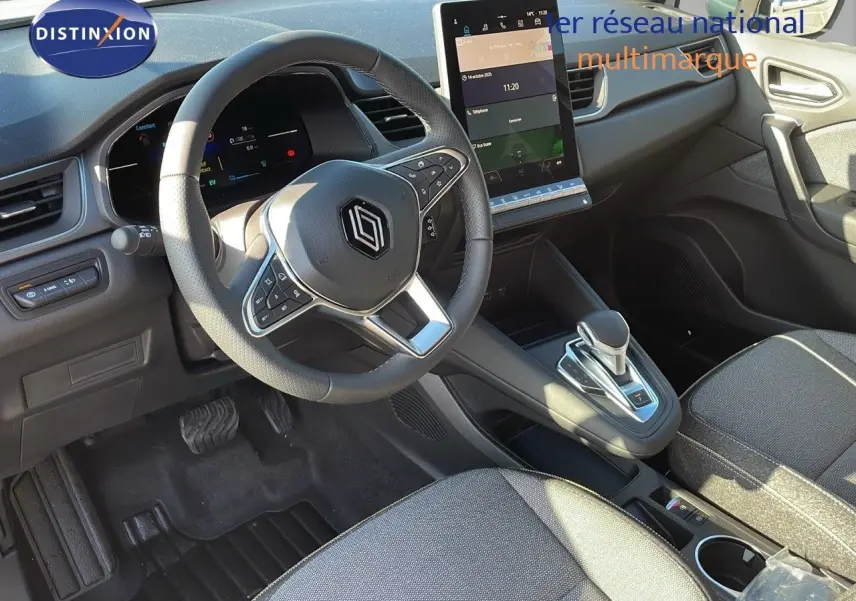 Vue intérieure du poste de conduite du Renault Captur E-Tech hybride 2025, volant multifonction et écran tactile vertical.