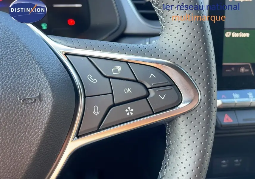 Détail des commandes au volant en cuir perforé du Renault Captur blanc nacré, version hybride 2025, avec écran tactile en arrière-plan.