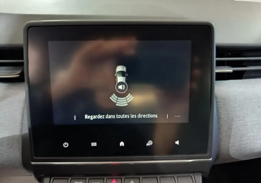 Écran tactile central affichant l’alerte de détection d’obstacles dans l’habitacle d’une Renault Clio gris clair.