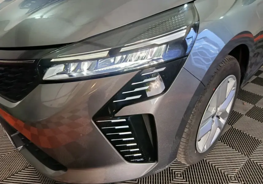 Gros plan sur l'avant droit de la Renault Clio gris clair 2025, mettant en valeur son phare LED et la jante moderne.