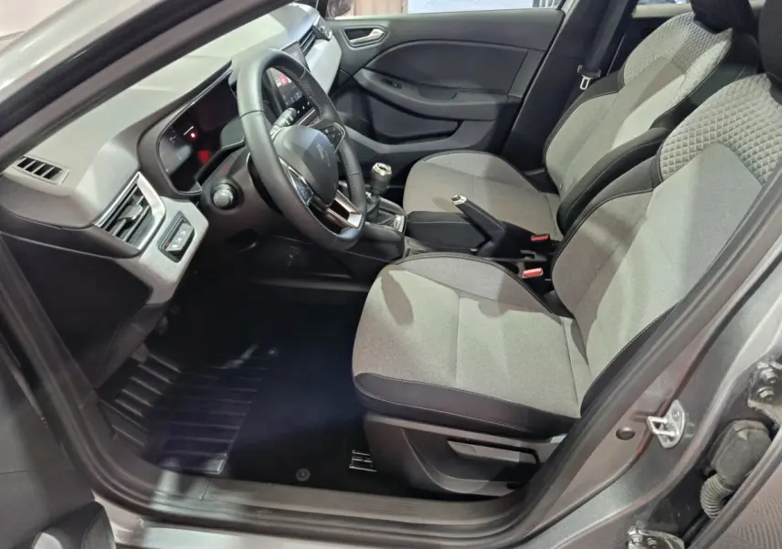 Vue intérieure côté conducteur de la Renault Clio gris clair 2025, volant multifonctions en cuir synthétique et sièges tissu gris.