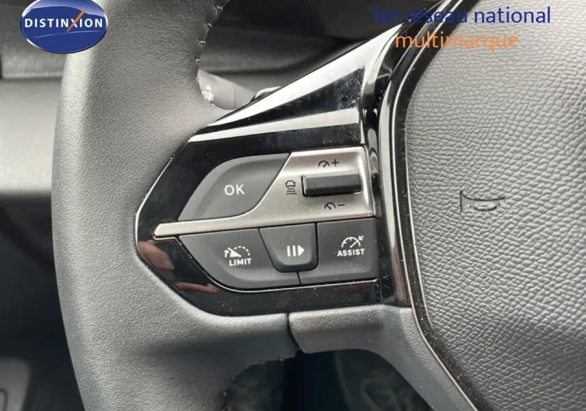Gros plan sur les commandes à gauche du volant noir du Peugeot 408 1.2 Hybrid 2025, avec boutons multifonctions visibles.