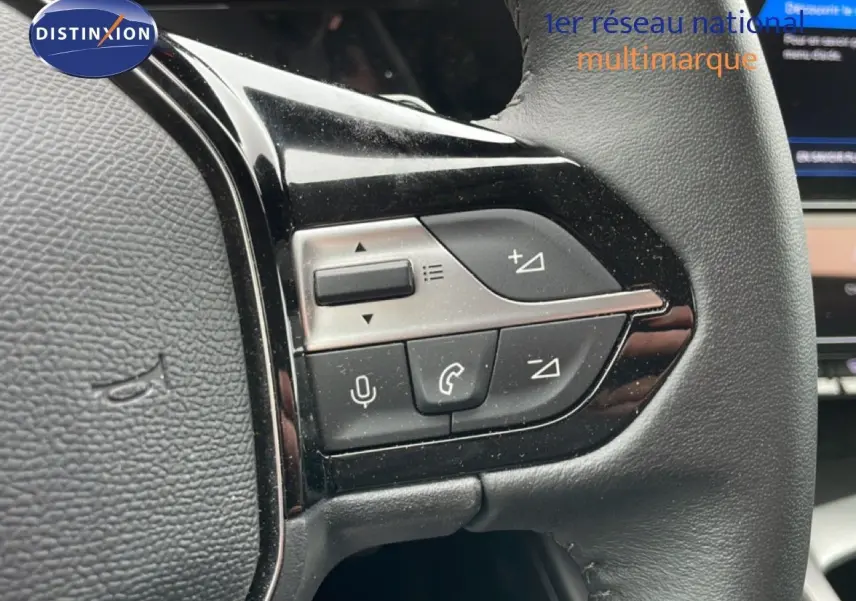 Gros plan sur les commandes multifonctions côté gauche du volant en cuir noir du Peugeot 408 gris Selenium 2025.