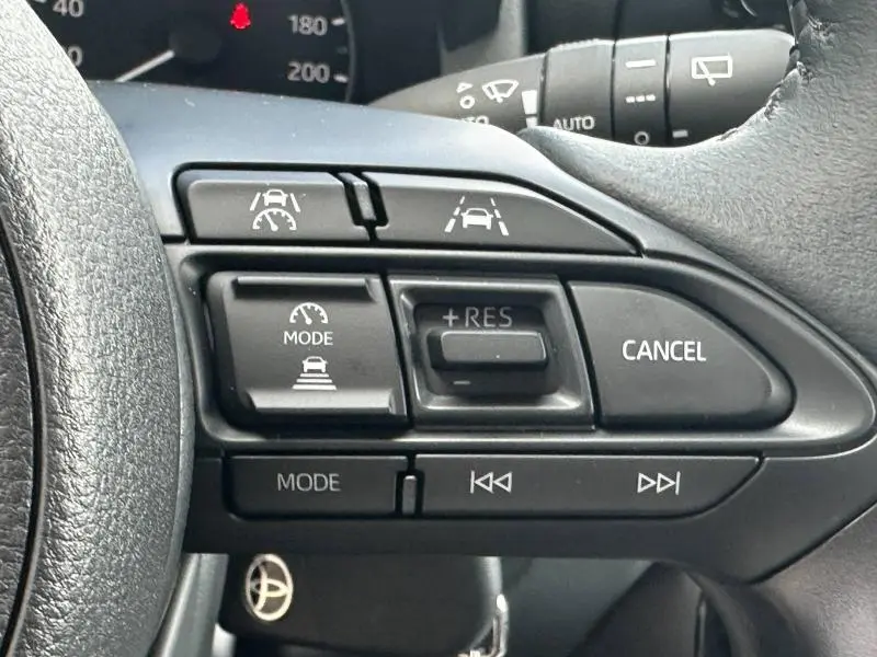 Gros plan sur les commandes au volant côté droit de la Toyota Yaris 116h Dynamic blanche, avec régulateur de vitesse et aides à la conduite.